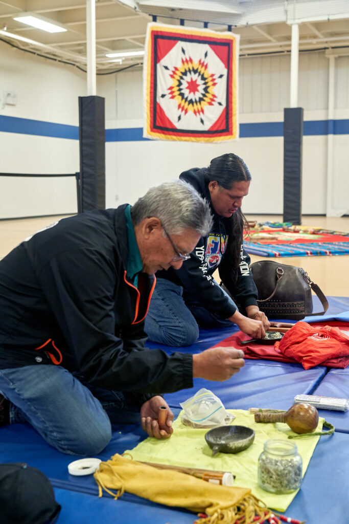 Two men kneel on a blanket and lay out what they will need for their pipe ceremony.